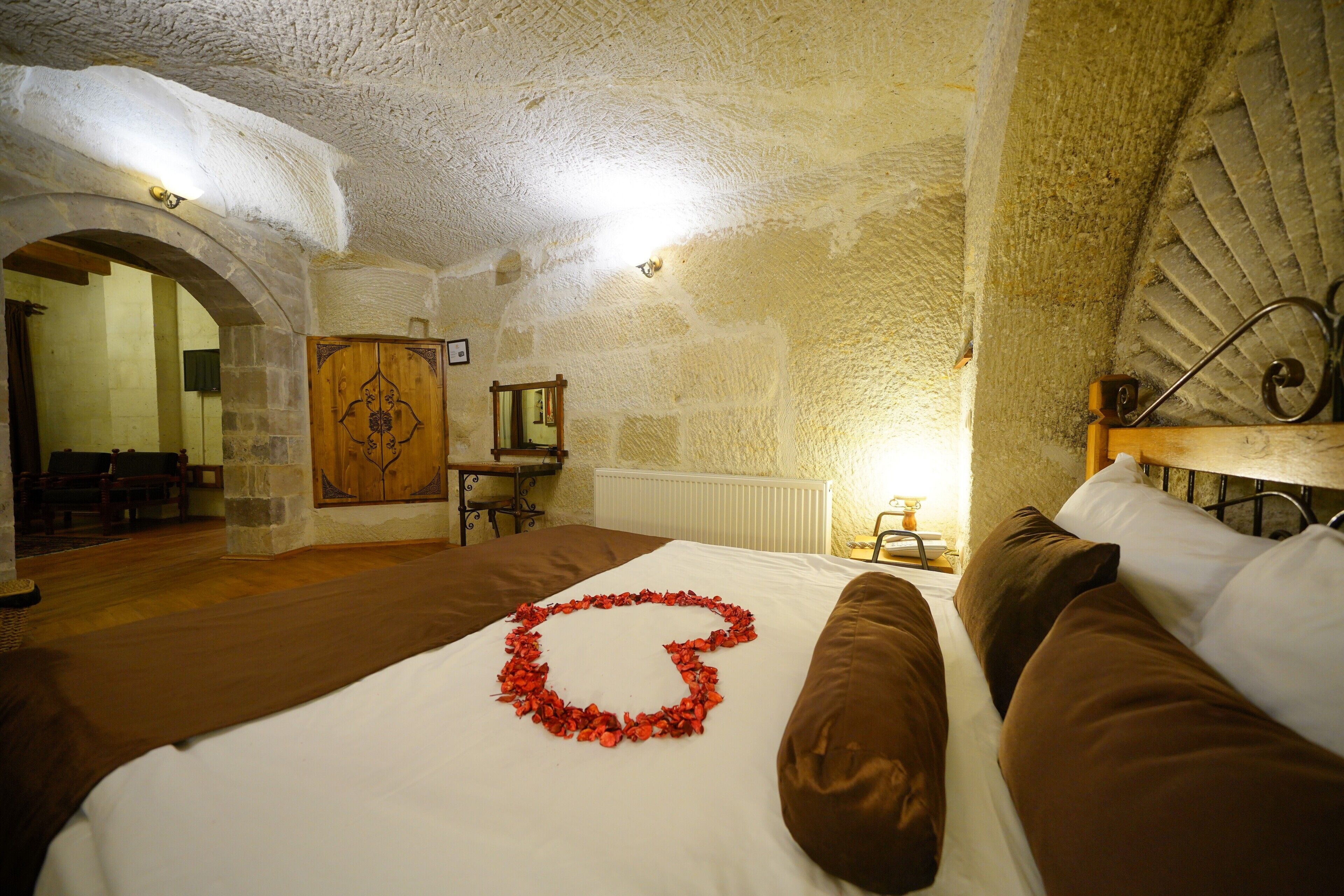 A bedroom with a stone ceiling, a bed with brown bedding, and a red flower arrangement on the bed.