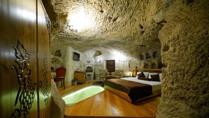 A cave-like bedroom with a bed, a small table, and a chair. - Harman Cave Hotel (Nevsehir)