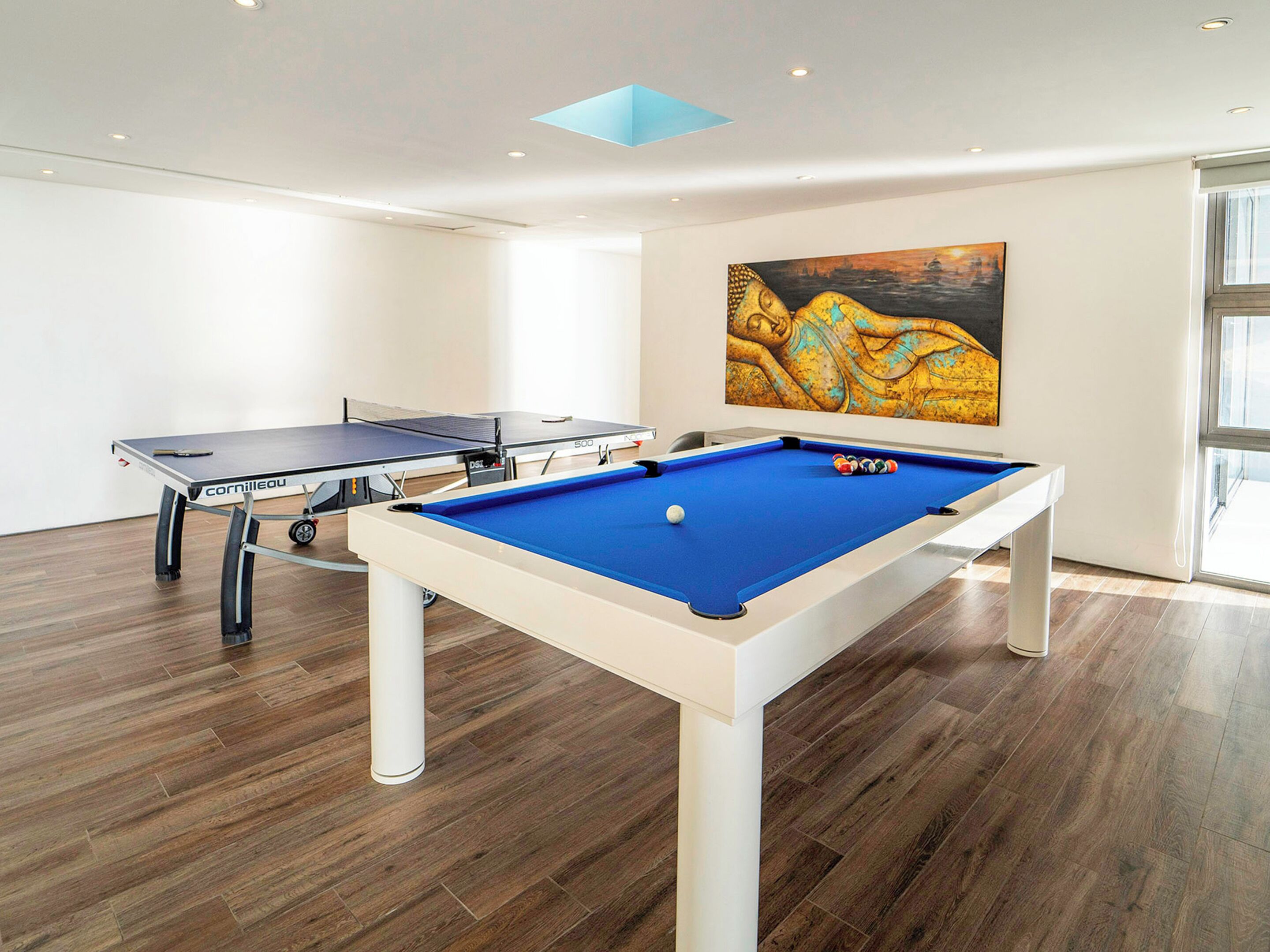 Una habitación con mesa de billar, mesa de tenis de mesa y un cuadro grande en la pared.