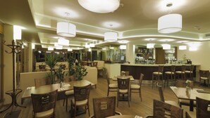Un restaurant doté de nombreuses tables et chaises, d’un bar et de plusieurs lampes suspendues.