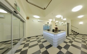 Un espace d’accueil avec un sol à carreaux, un comptoir de réception, une horloge et un escalier.