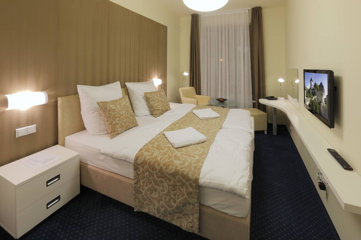 Een hotelkamer met een groot bed, nachtkastjes, een bureau met stoel, een televisie en een afstandsbediening.