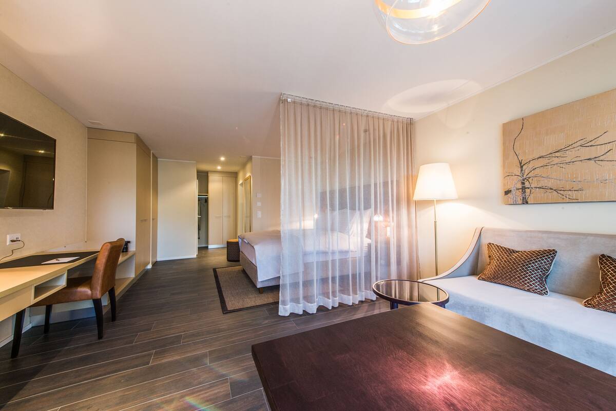 Ein Hotelzimmer mit einem Bett, einem Schreibtisch, einem Sessel, einer Couch, einer Lampe und einem Bild an der Wand.