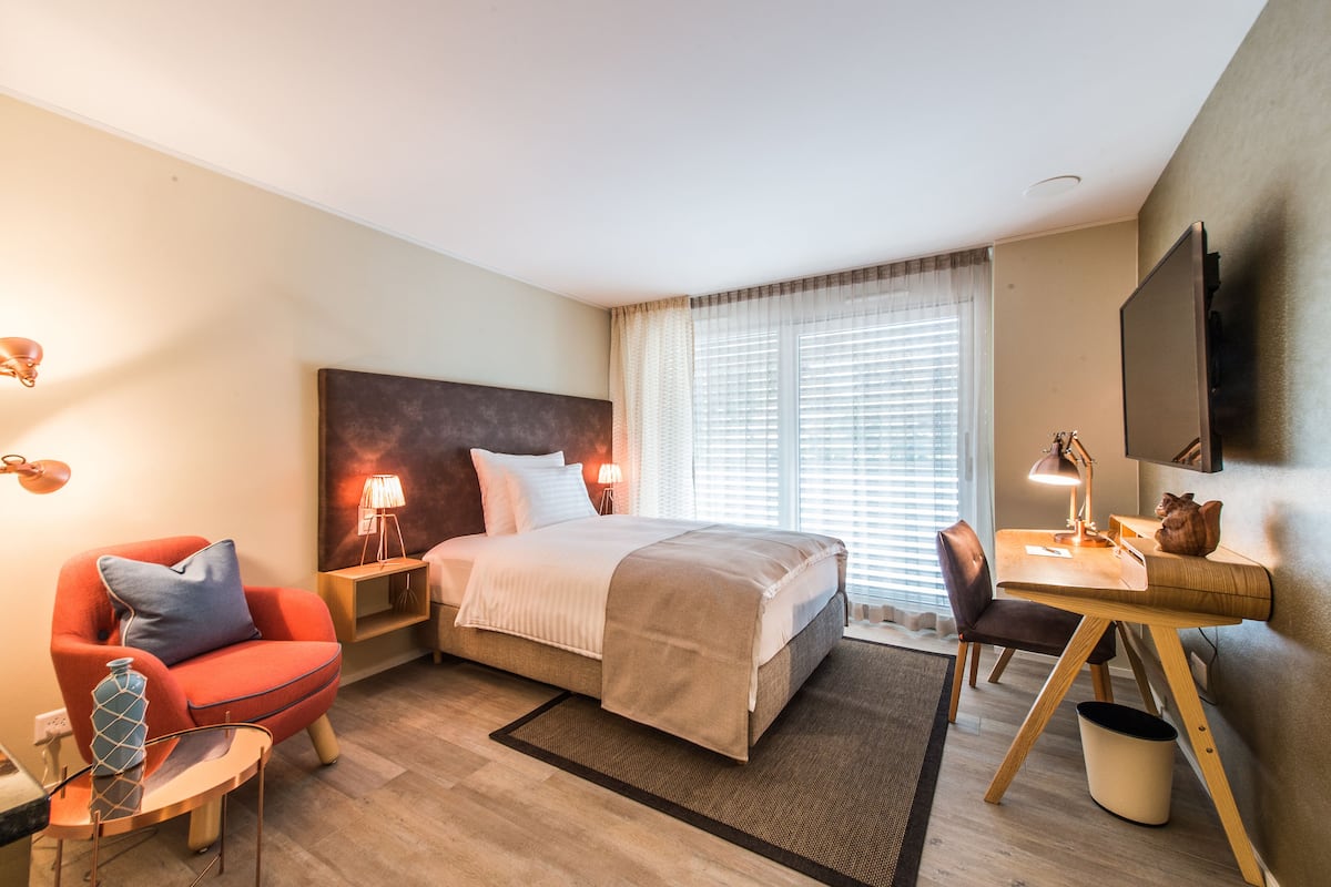 Ein modernes Hotelzimmer mit Bett, Schreibtisch, Stuhl, Lampe und Fernseher.