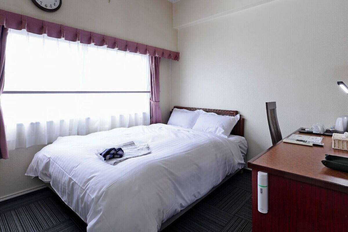 Une chambre d’hôtel avec un lit, un bureau, une horloge et une fenêtre avec des rideaux.