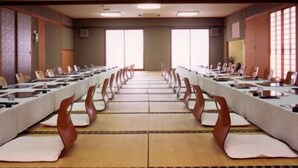 A conference room with long tables and chairs, large windows, and a tiled floor.