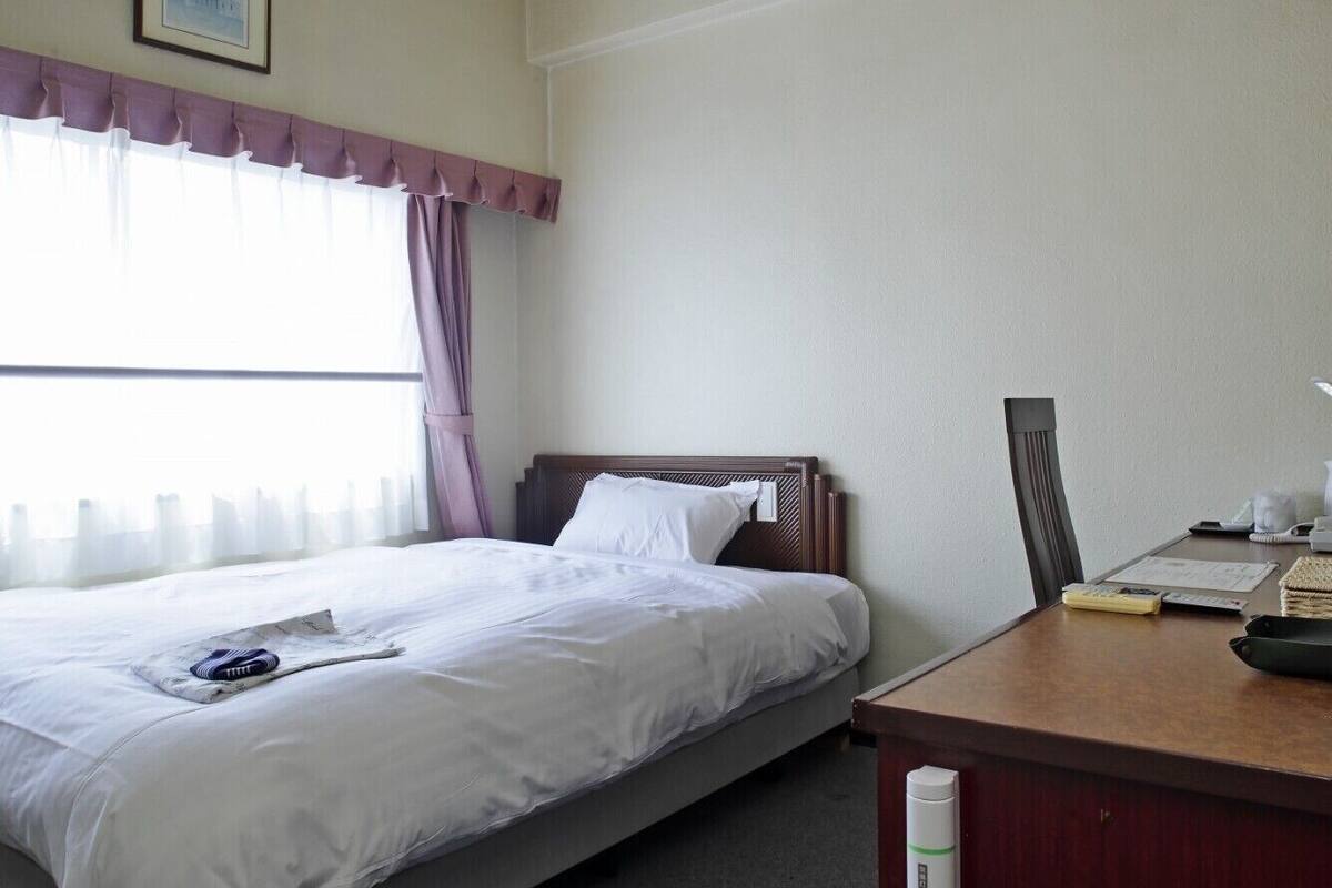 Une chambre d’hôtel avec un lit, un bureau et une fenêtre avec des rideaux.