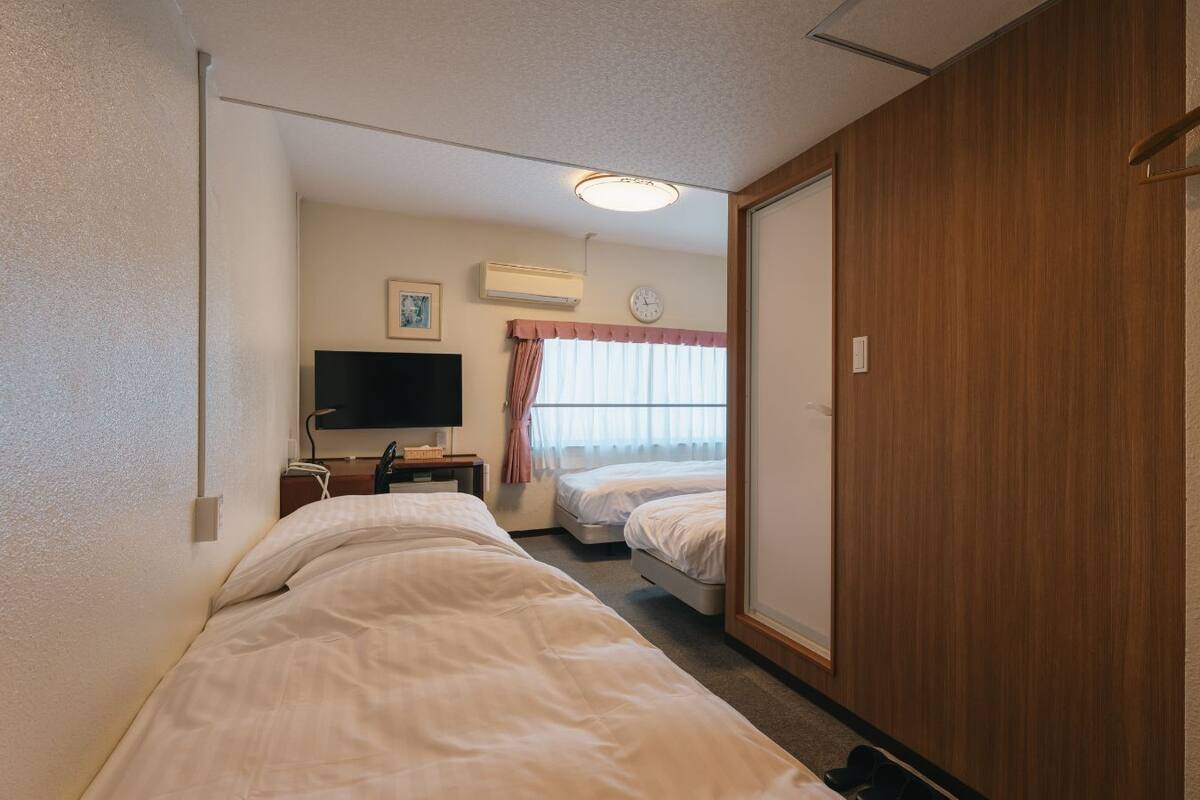 Une chambre d’hôtel avec deux lits, une télévision, un appareil de climatisation, une horloge et une armoire en bois.