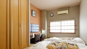 A hotel room with two beds, a desk with a chair, a clock, and an air conditioning unit.