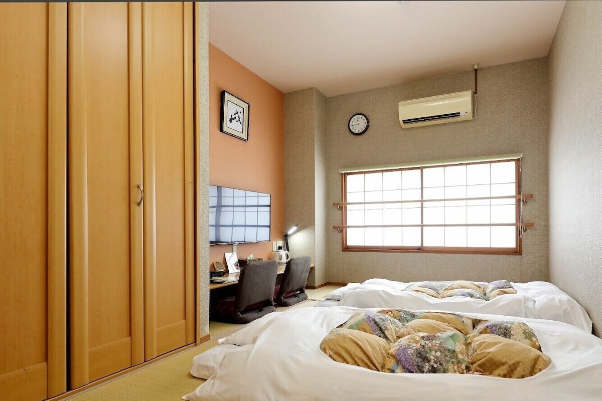 Une chambre d’hôtel avec deux lits, un bureau avec une chaise, une horloge et un appareil de climatisation.