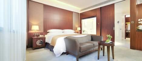 A hotel room with a bed, a sofa, a bedside table, and a small table with a plant.