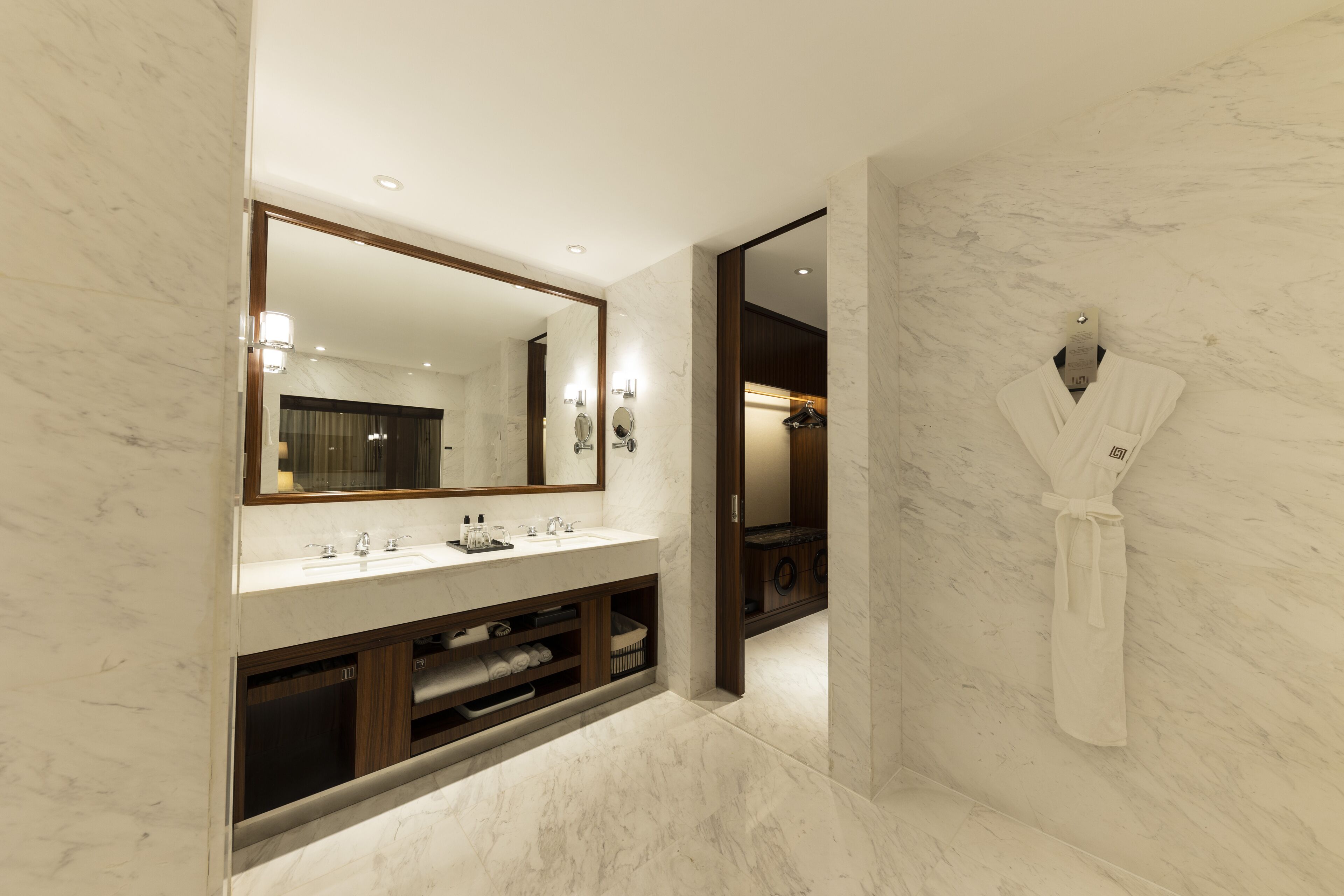 A modern bathroom with a large mirror, marble walls, a vanity with a sink, and a robe hanging on the wall.
