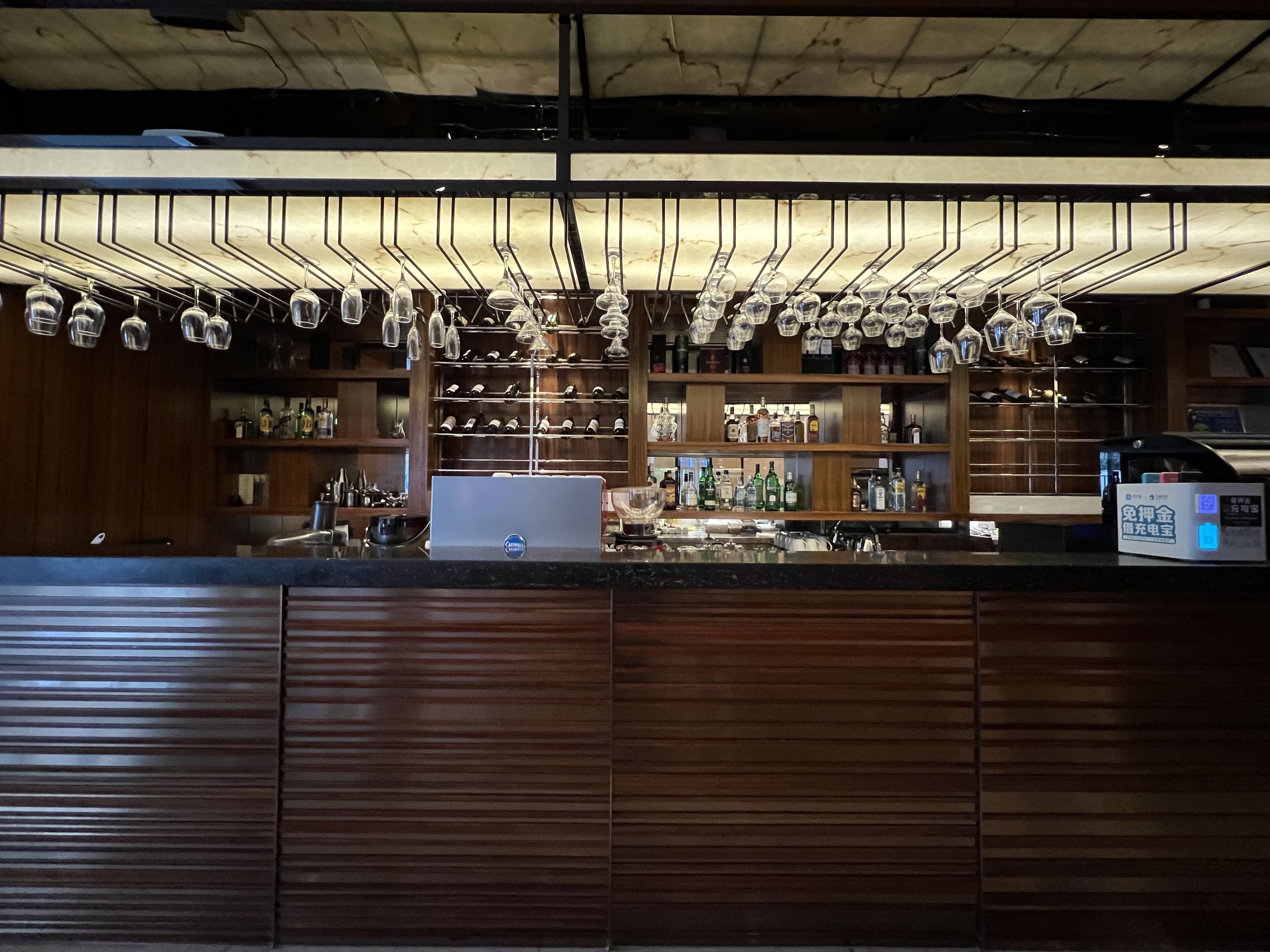 A bar area with a marble ceiling, wine glasses hanging from the ceiling, and shelves stocked with bottles and glasses.