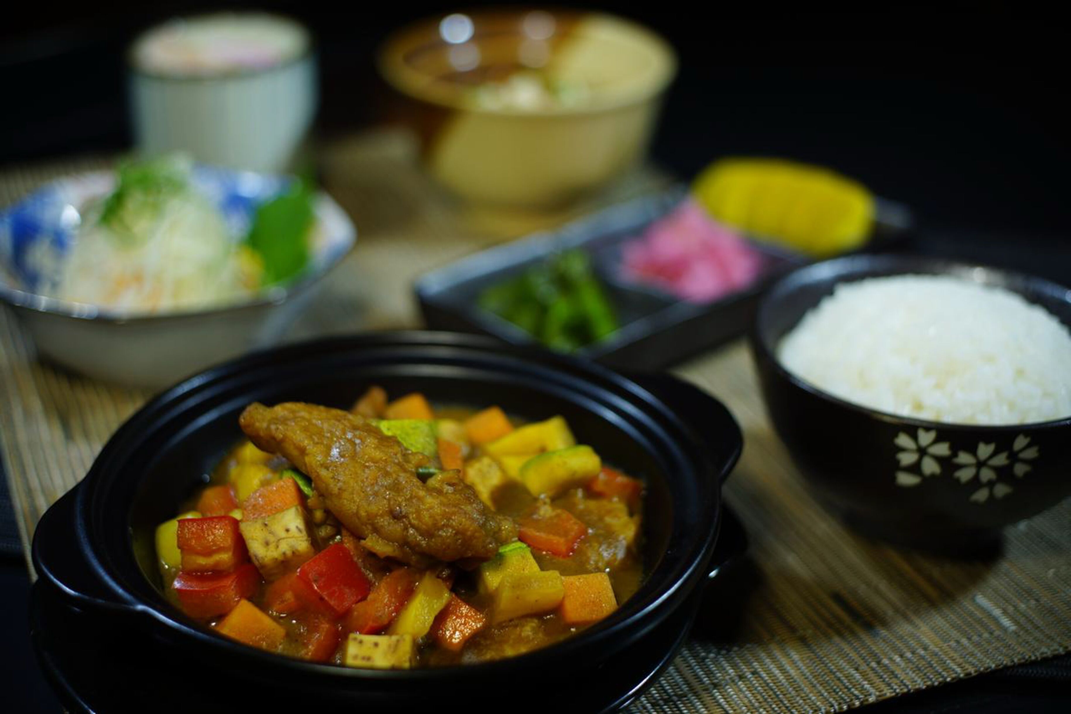A meal with a bowl of rice, a bowl of soup with vegetables and meat, and a small dish of pickled vegetables.