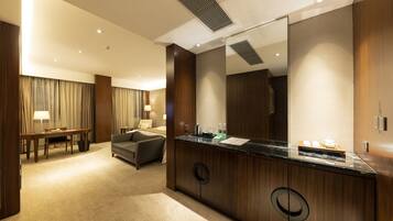 Ein Hotelzimmer mit einem großen Bett, einer Sitzecke mit Tisch und Stühlen, einem Badezimmer mit großem Spiegel und Waschbecken sowie einem Teppichboden.
