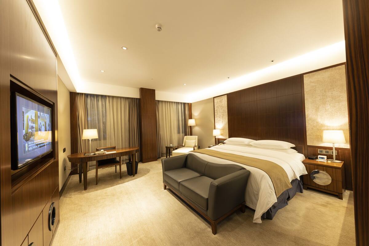 A hotel room with a bed, a sofa, a desk, and a TV.
