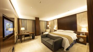 A hotel room with a bed, a sofa, a desk, and a TV.