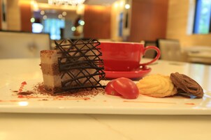 A dessert plate with a slice of cake, a cherry, and a chocolate pastry on a white plate.