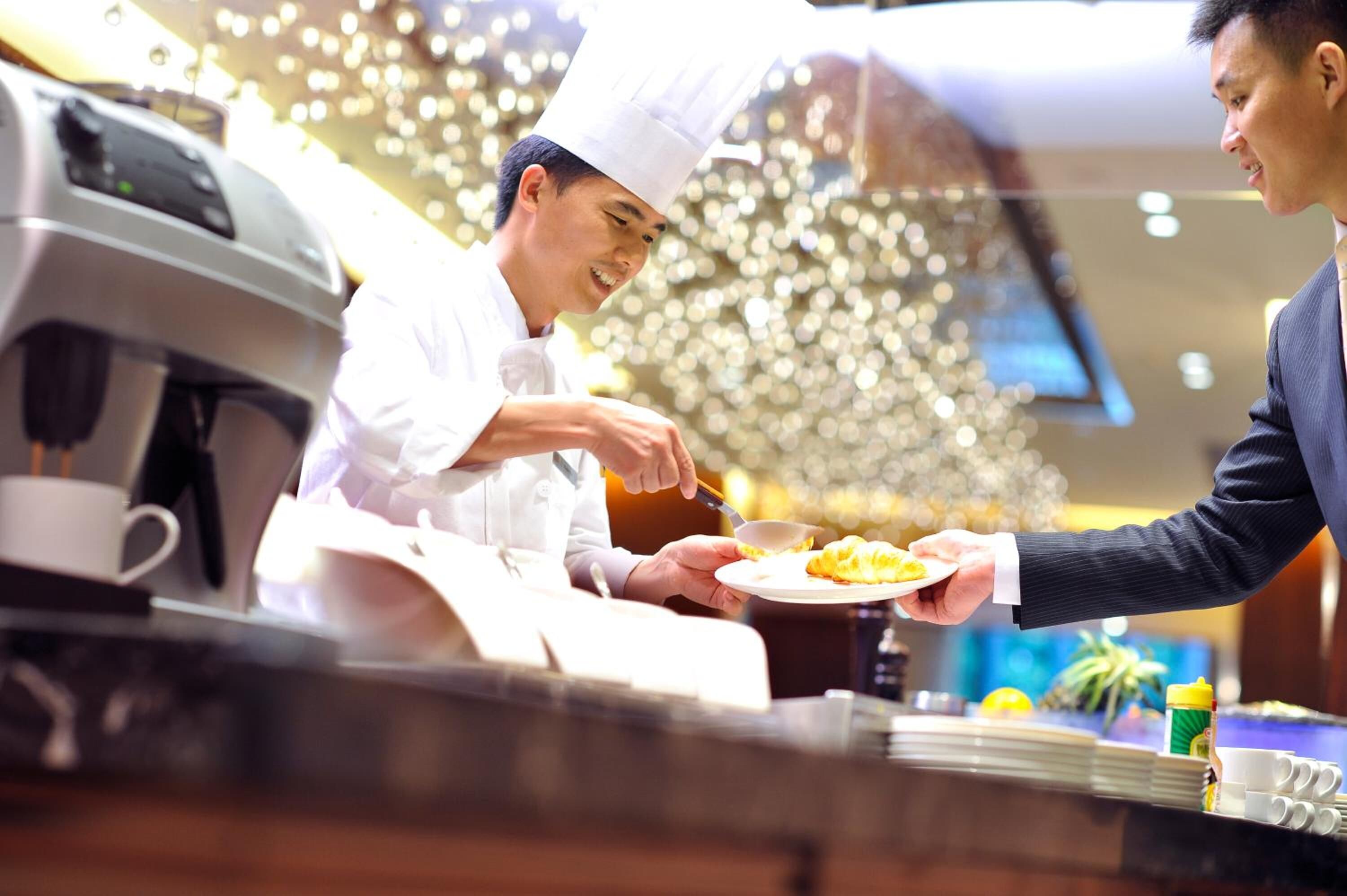 A chef serving food to a guest in a well-lit, modern restaurant setting.