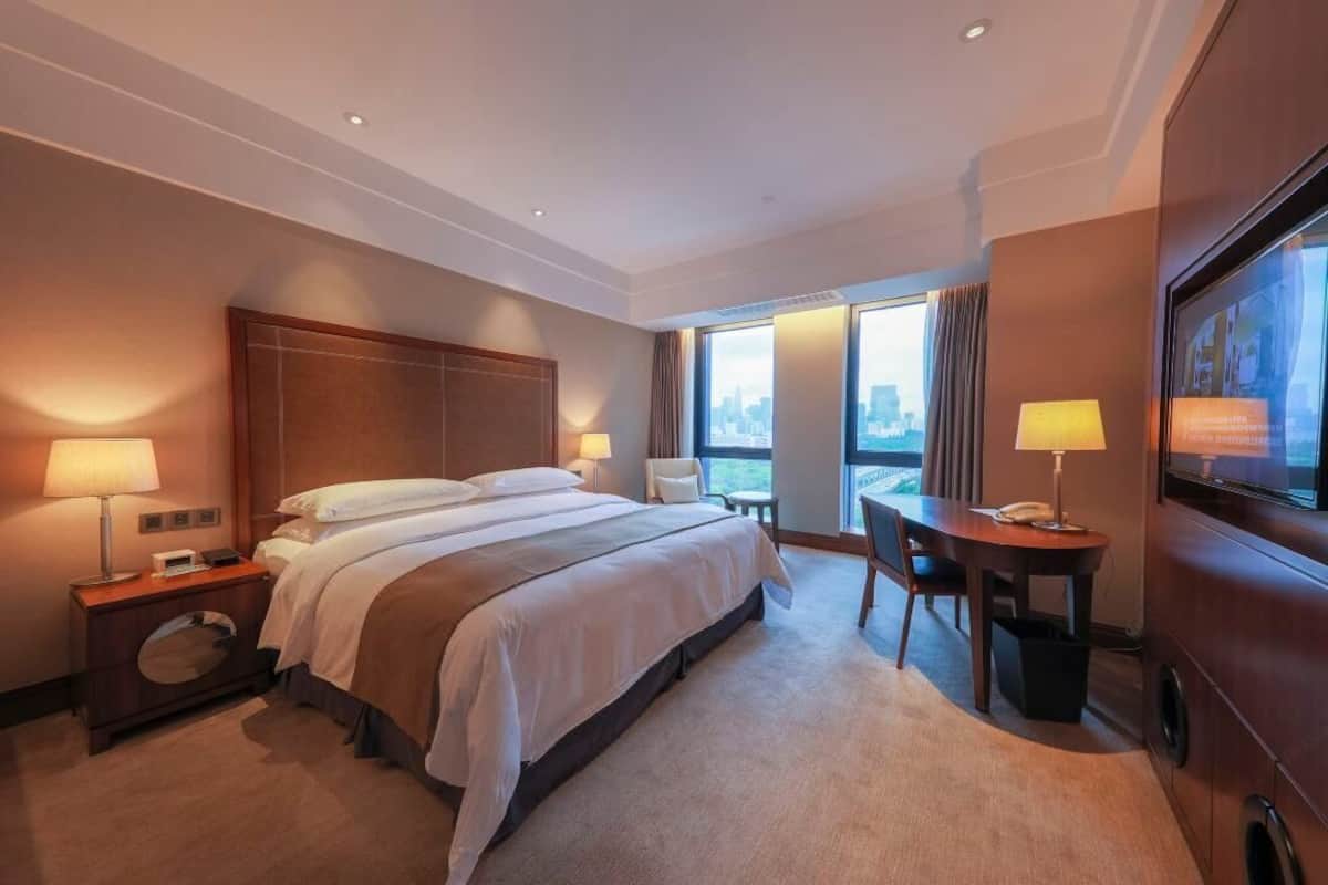 A hotel room with a large bed, bedside tables, a desk, and a television.