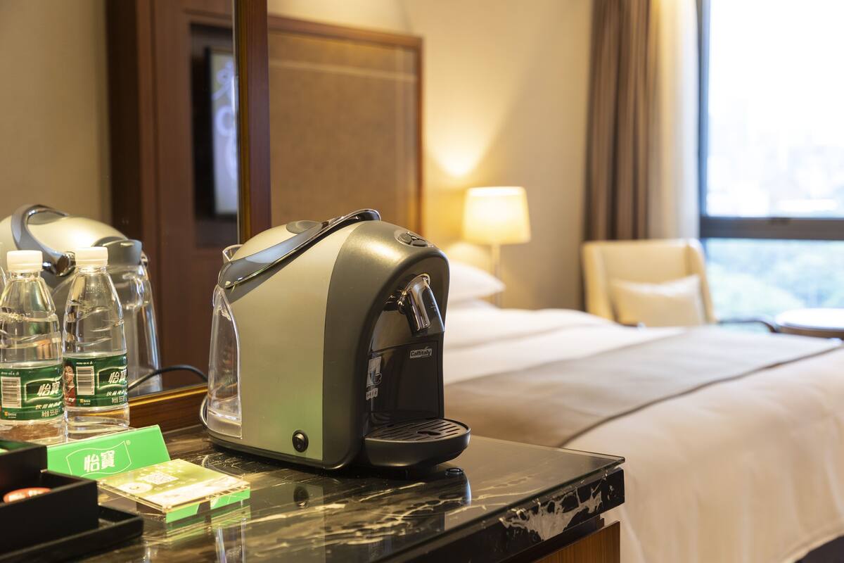 A hotel room with a bed, a coffee machine, and bottled water on the counter.