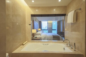 A modern bathroom with a large mirror, a bathtub, and a view of a bedroom with a bed and curtains.