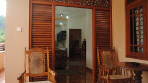 A traditional wooden door with intricate carvings, leading to a room with a tiled floor and a small table with a chair. - Kumara Guesthouse Unawatuna (Unawatuna)