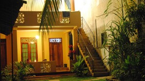 A building with a staircase leading to a wooden door, surrounded by greenery and a well-maintained lawn. - Kumara Guesthouse Unawatuna (Unawatuna)