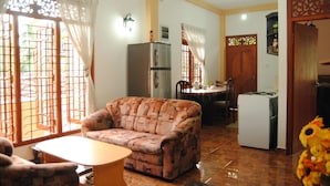 A living room with a sofa, a dining table, and chairs. There is a kitchen area with a refrigerator and a stove. - Kumara Guesthouse Unawatuna (Unawatuna)