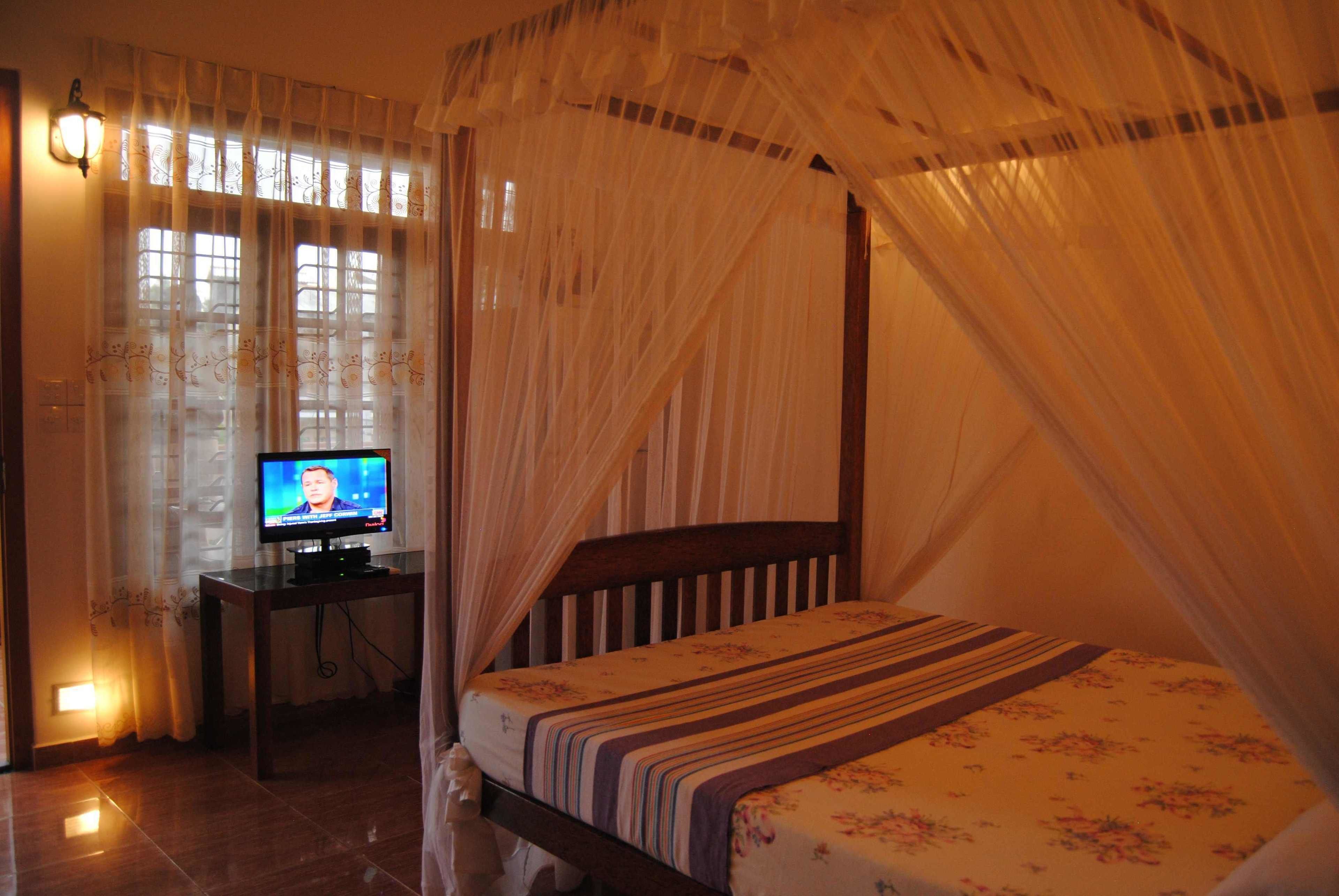 Ein Schlafzimmer mit einem Bett, einem Fernseher auf einem Schrank und einem Fenster mit Vorhängen.