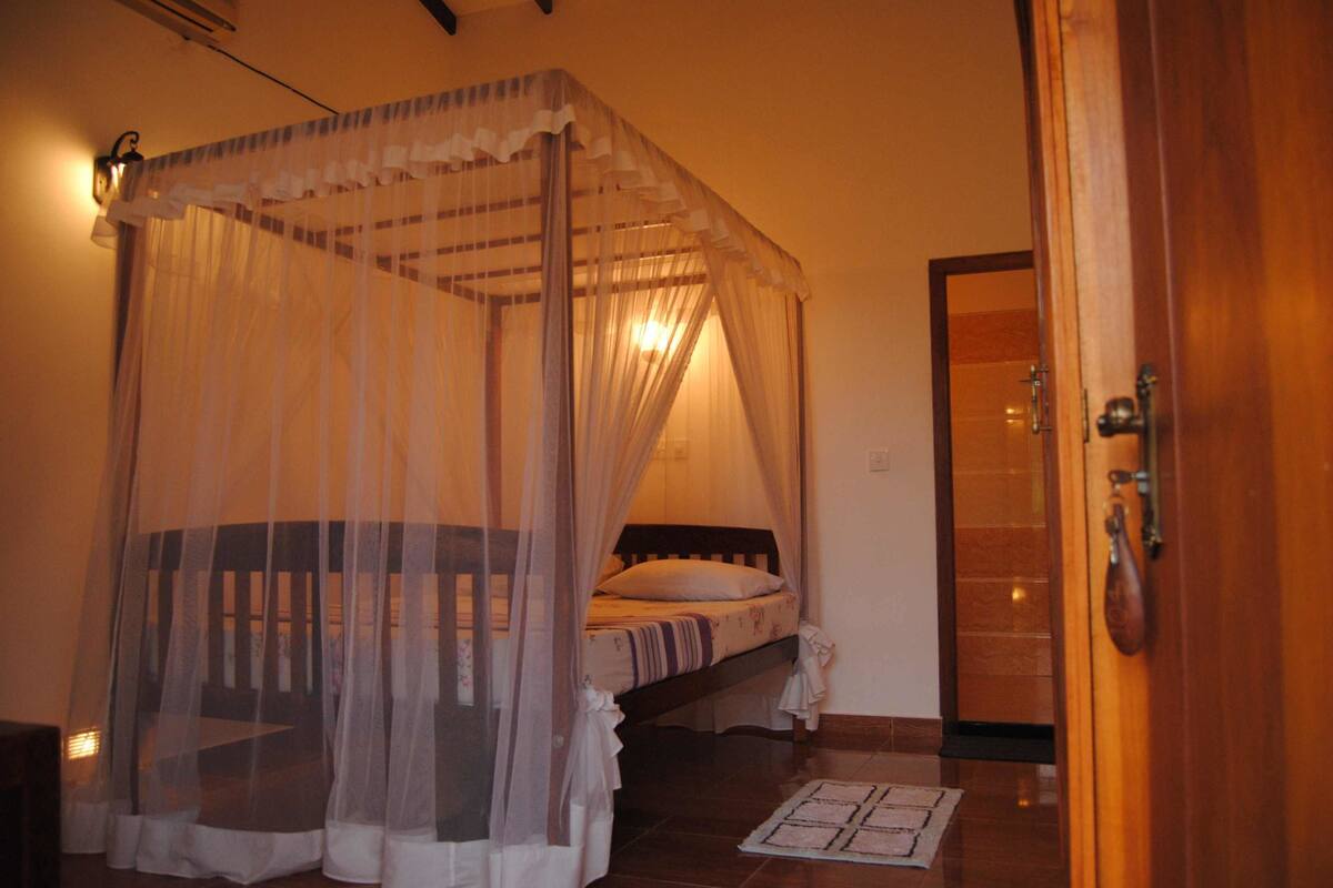 Een slaapkamer met een hemelbed, een houten deur en een betegelde vloer.