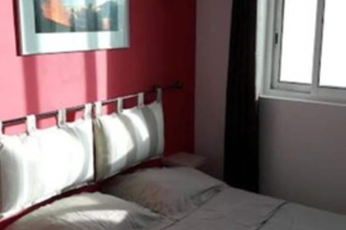 A bedroom with a bed, a window, and a painting on the wall.