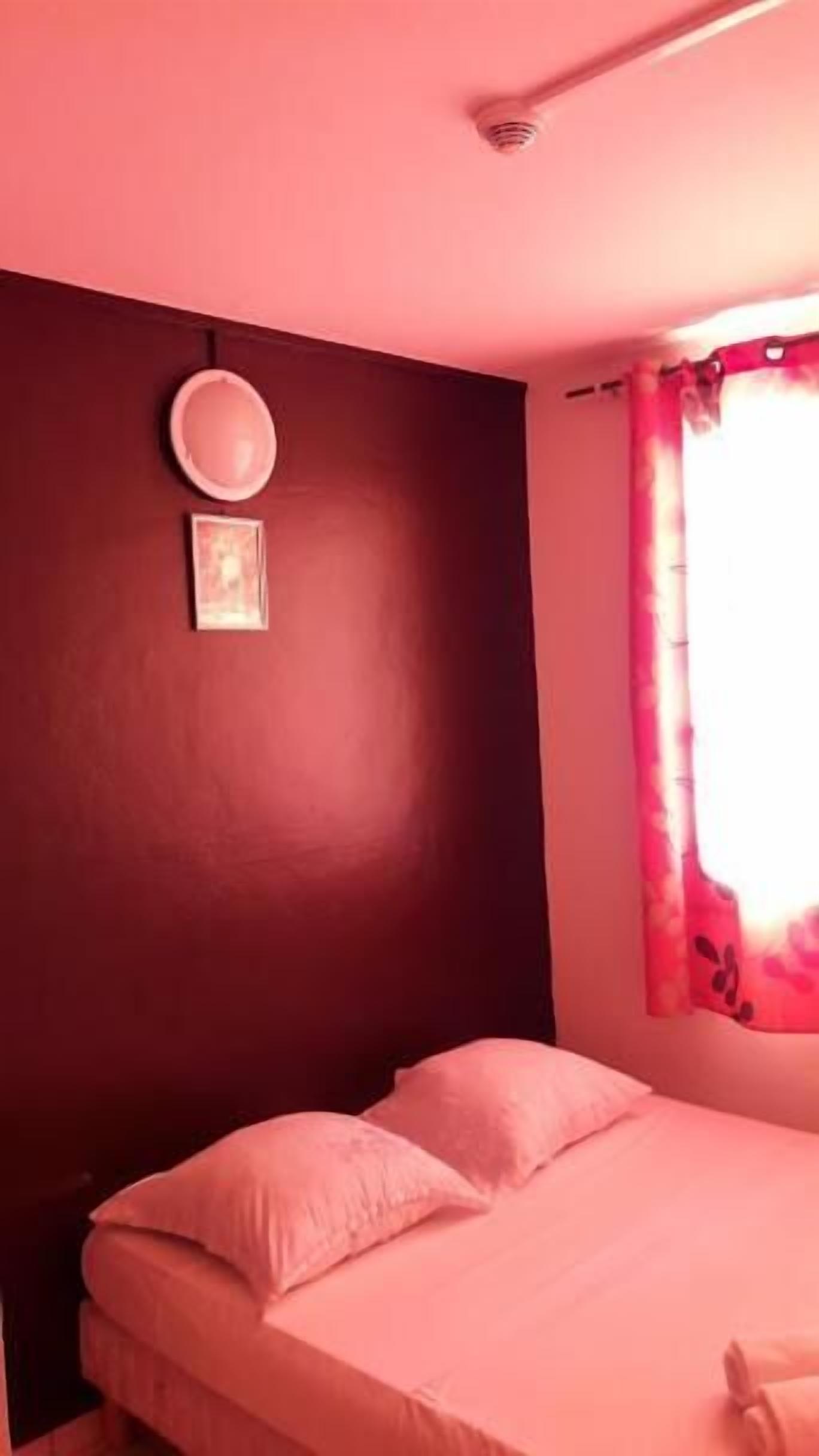 Une pièce avec un lit, un luminaire fixé au mur et une fenêtre avec un rideau.