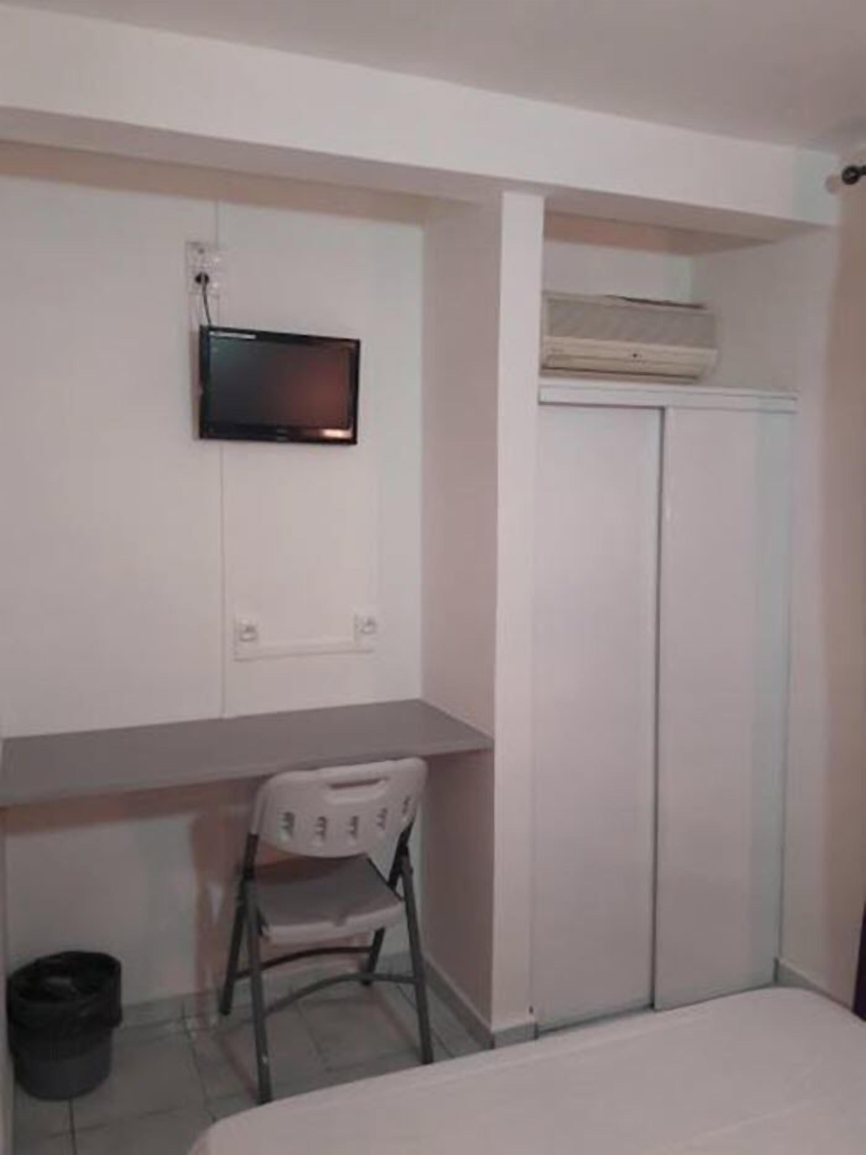 A bedroom with a bed, a desk, a chair, a TV mounted on the wall, and a wardrobe.