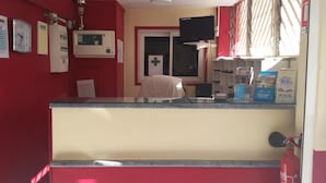 A reception area with a counter, a clock, a first aid sign, a television, and a fire extinguisher. - Hotel Du Centre (Saint-Denis)