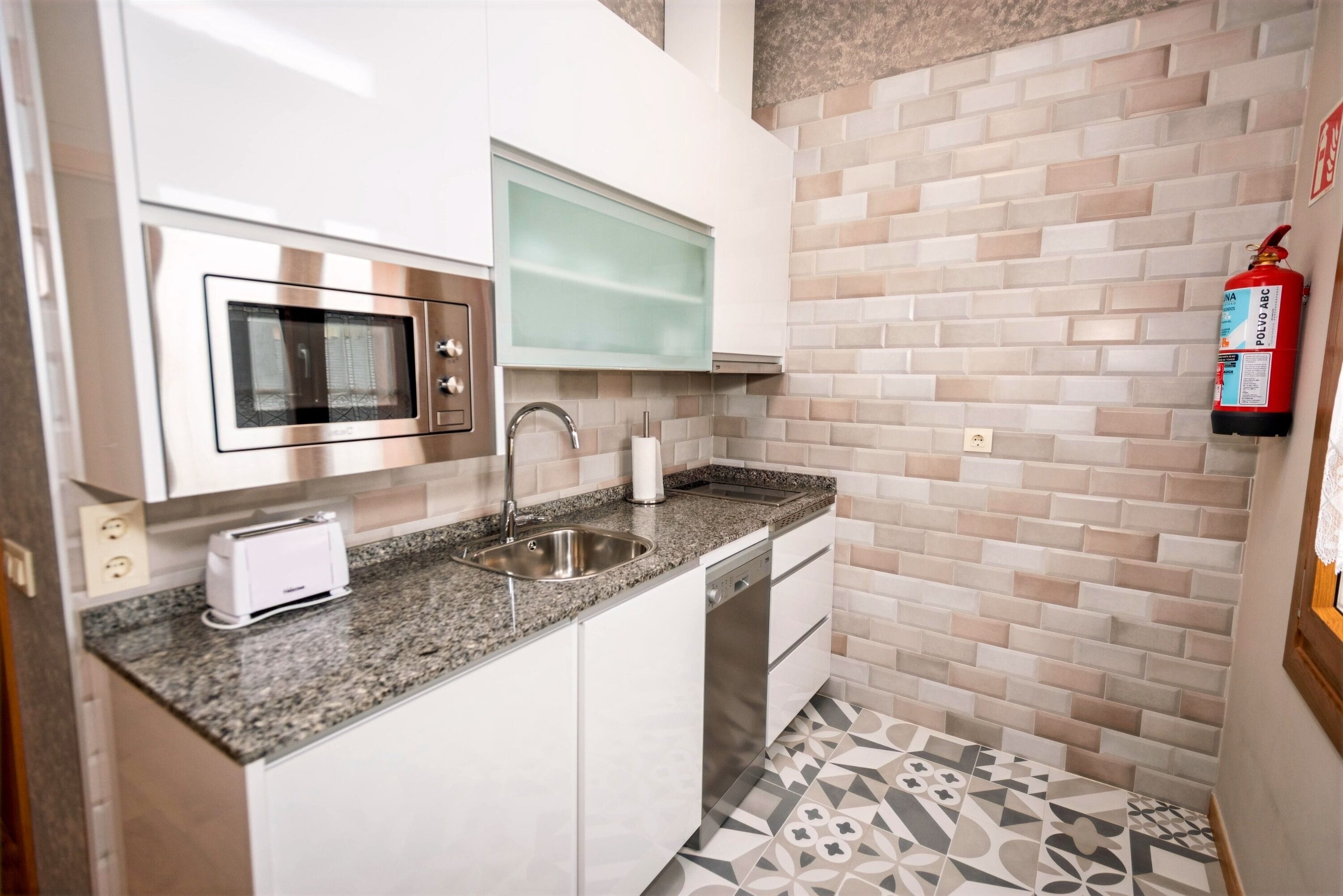 A compact kitchen with a microwave, toaster, sink, and dishwasher.