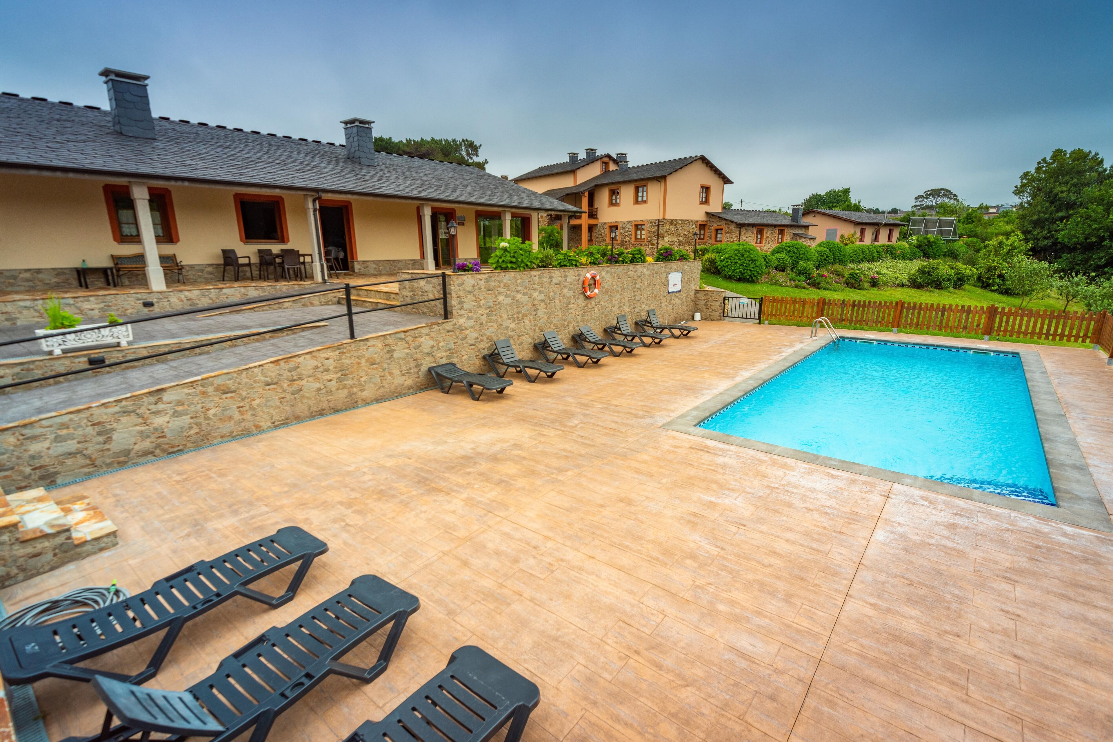 A pool area with lounge chairs, a lifebuoy, and a stone wall.