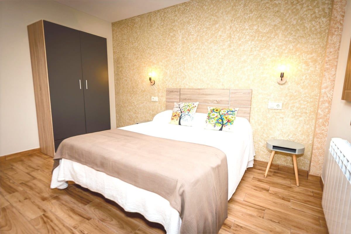 Un dormitorio con cama, armario de madera, mesitas de noche y una pequeña mesa.