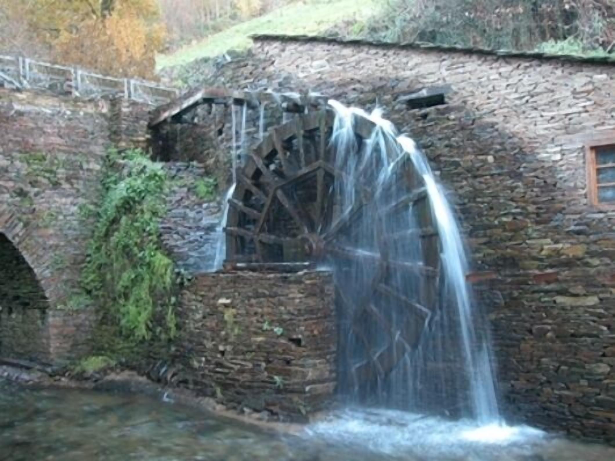 Un molino de agua de piedra con una rueda de madera y un pequeño arroyo que fluye desde él.