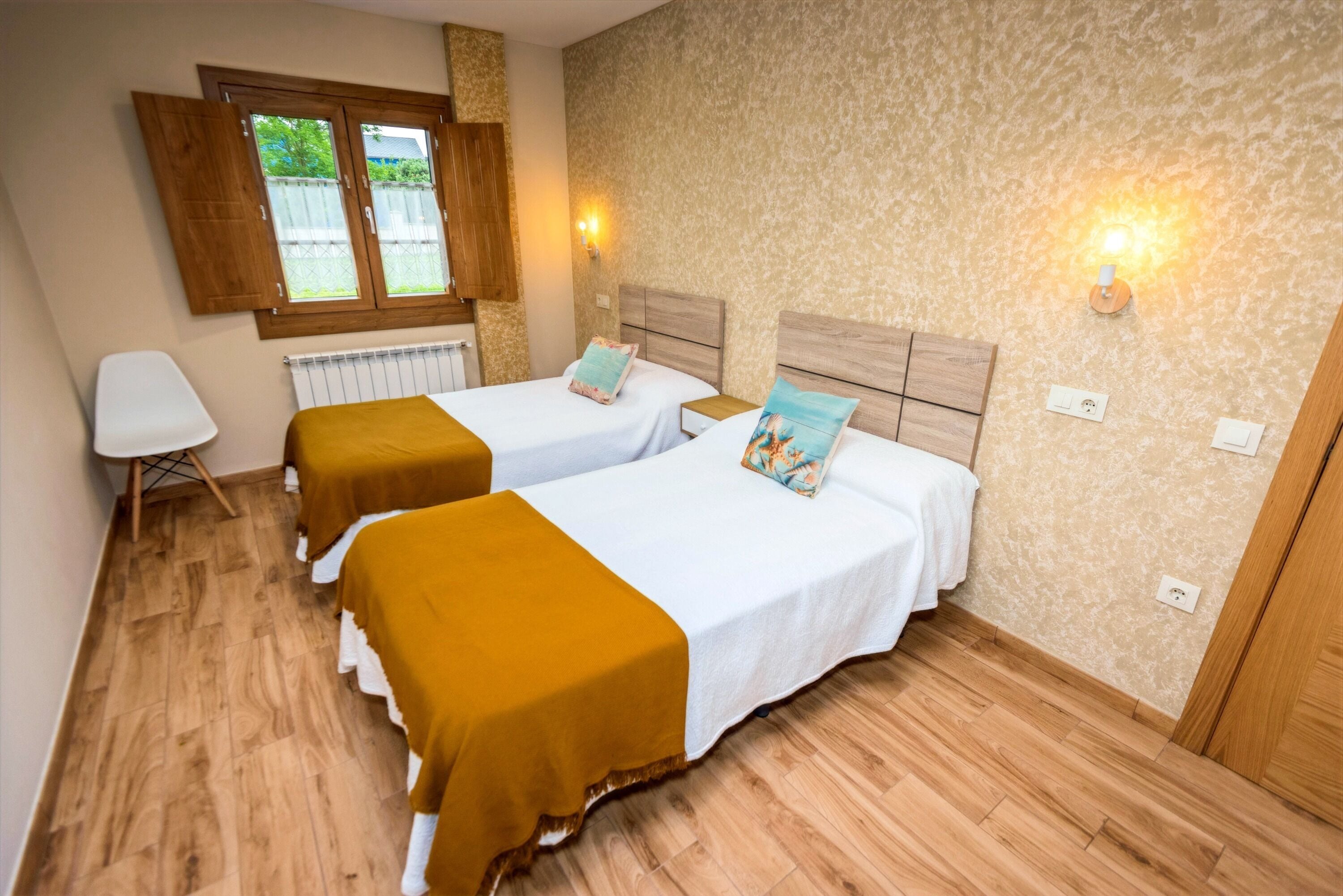 A room with two beds, a radiator, a window with wooden shutters, and wall-mounted lights.