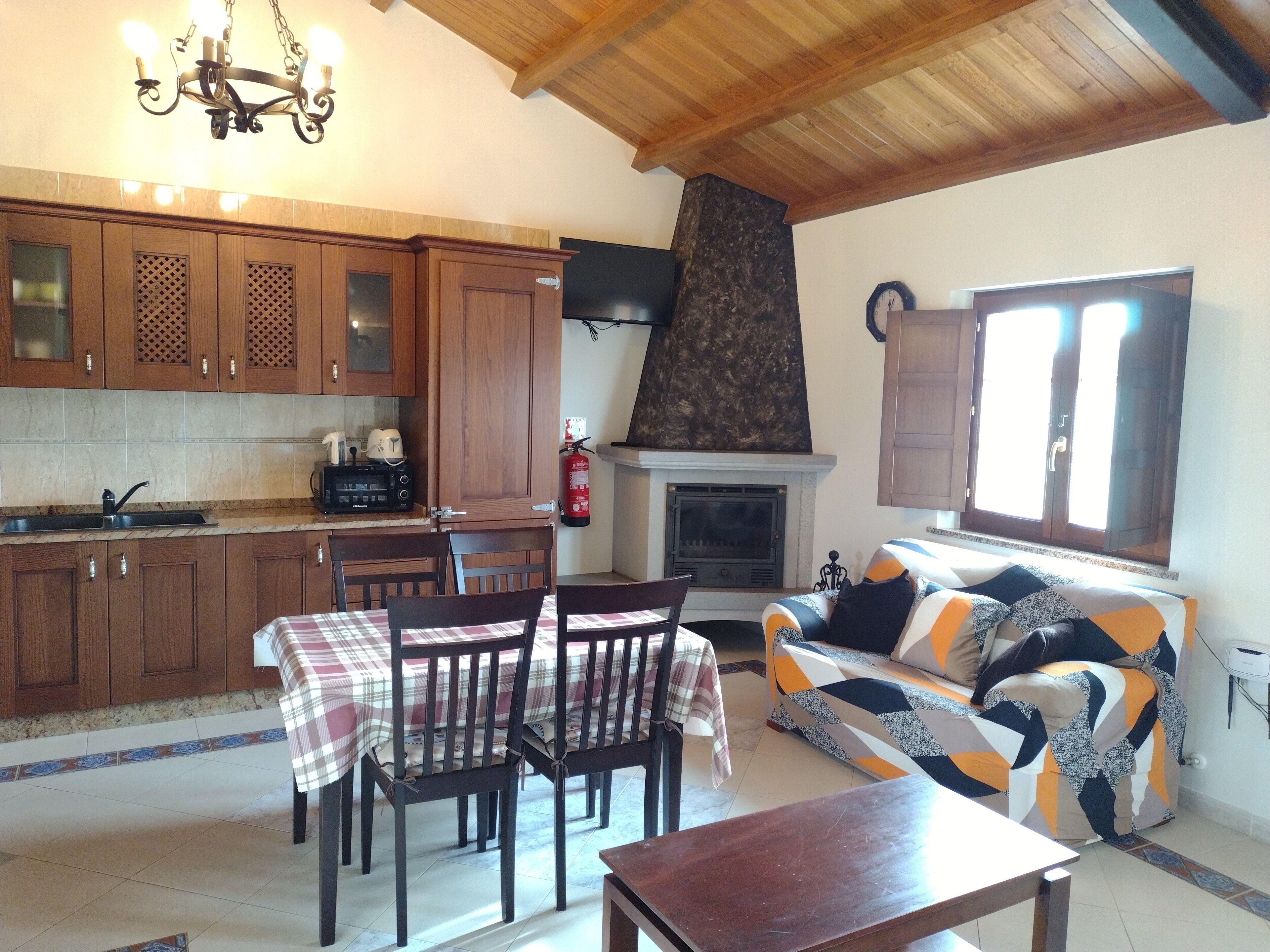 Ein gemütliches Wohnzimmer mit Kamin, einer Couch mit gemusterten Kissen und einem Essbereich mit Tisch und Stühlen.
