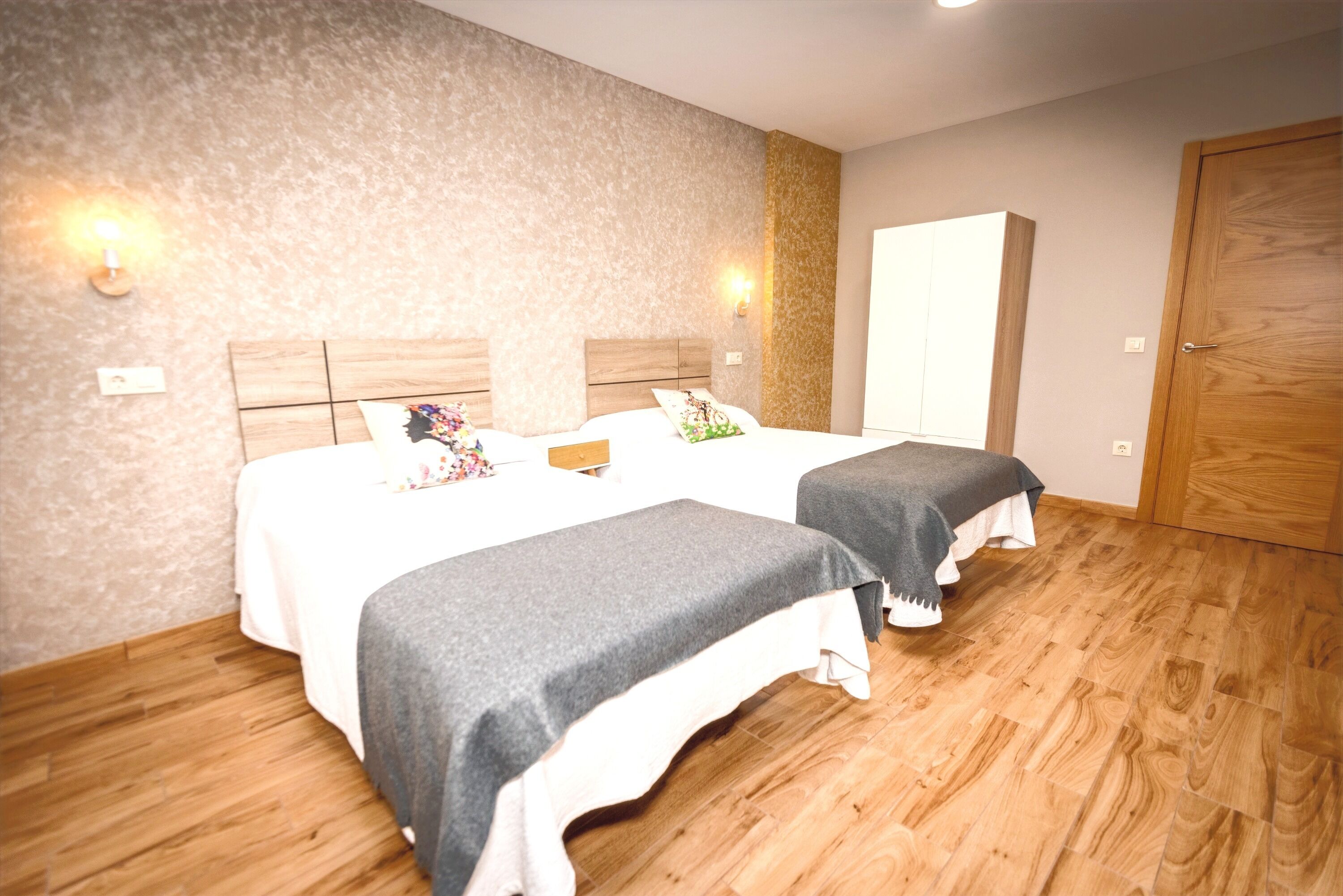 Een hotelkamer met twee bedden, houten vloeren en een grote kledingkast.
