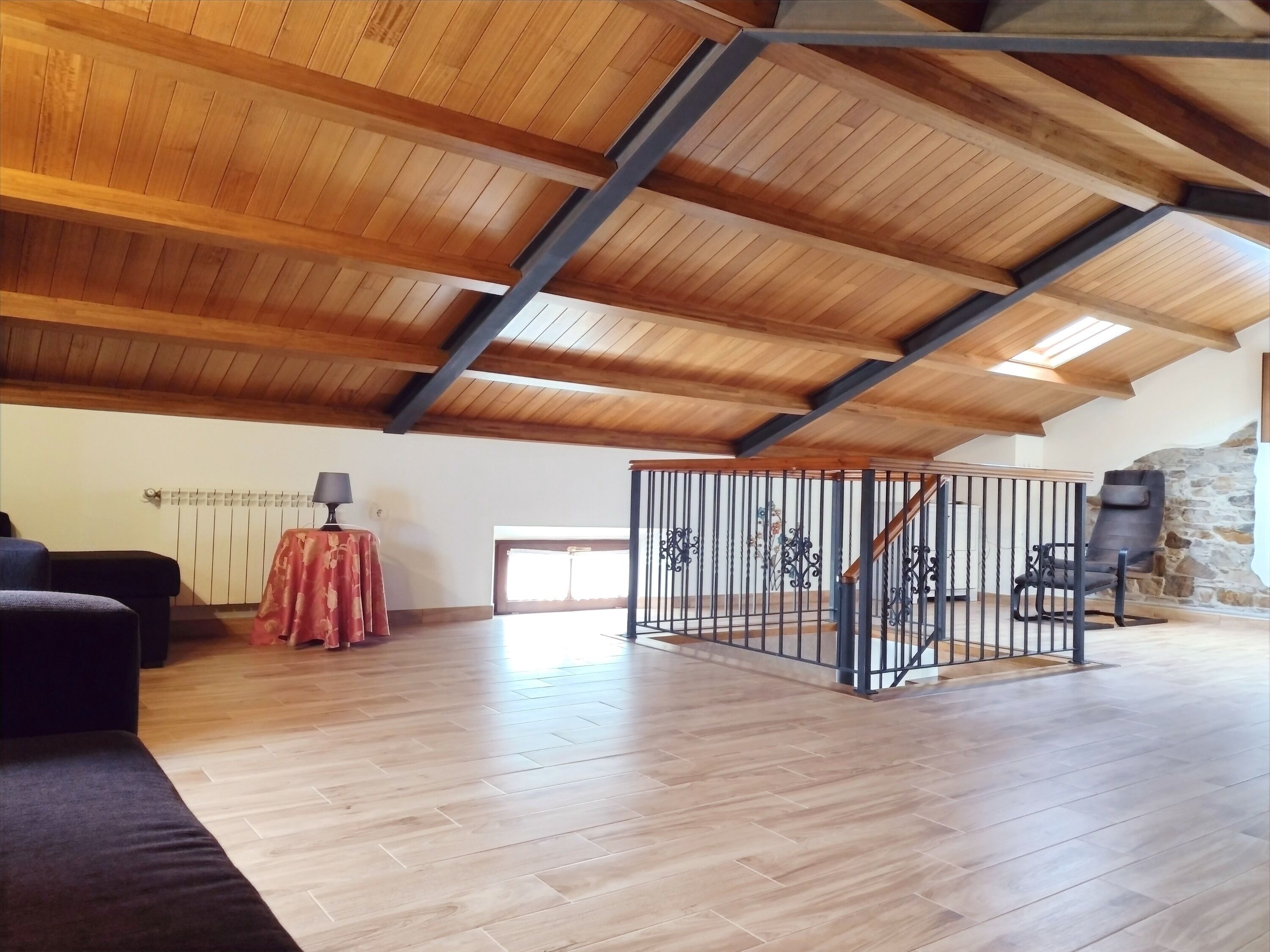 A spacious loft with wooden beams, a stone wall, and a staircase.