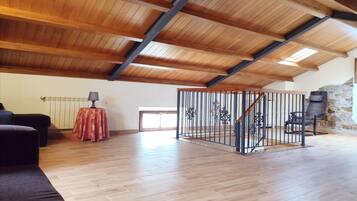 A spacious loft with wooden beams, a stone wall, and a staircase.