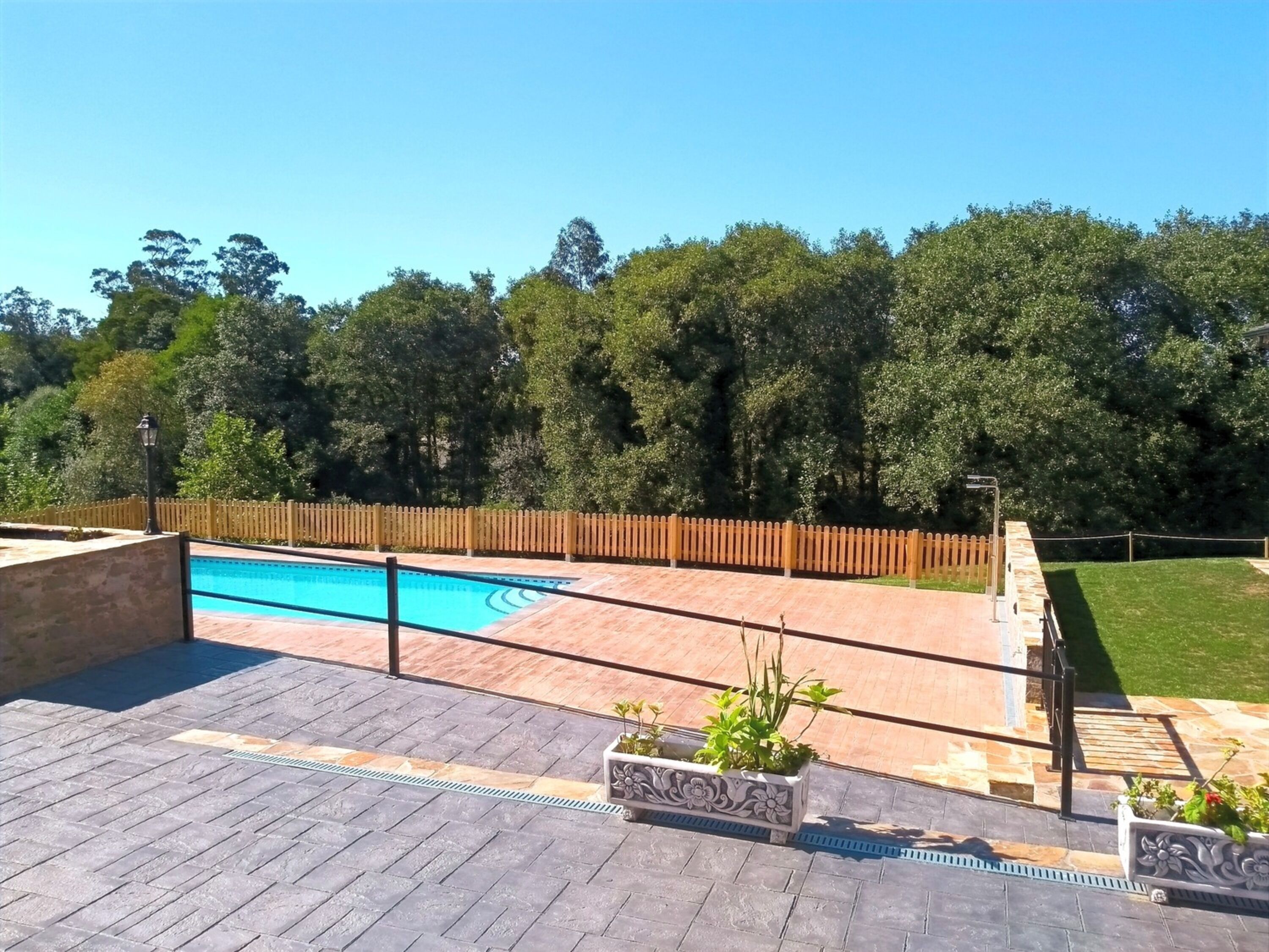 Una piscina con cerco de madera, rodeada por un patio empedrado y plantas en macetas.