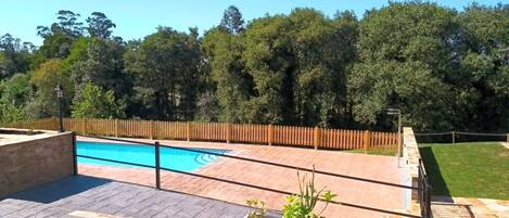 Una piscina con cerco de madera, rodeada por un patio empedrado y plantas en macetas.