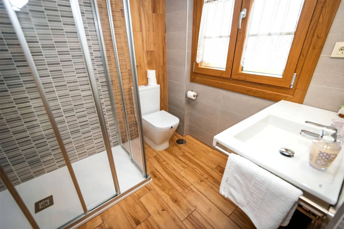 Un baño con ducha, inodoro, lavabo y suelo de madera.