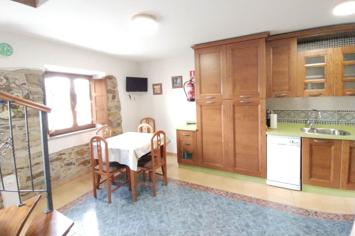 Una cocina con armarios de madera, una mesa de comedor con sillas, un televisor y un extintor.