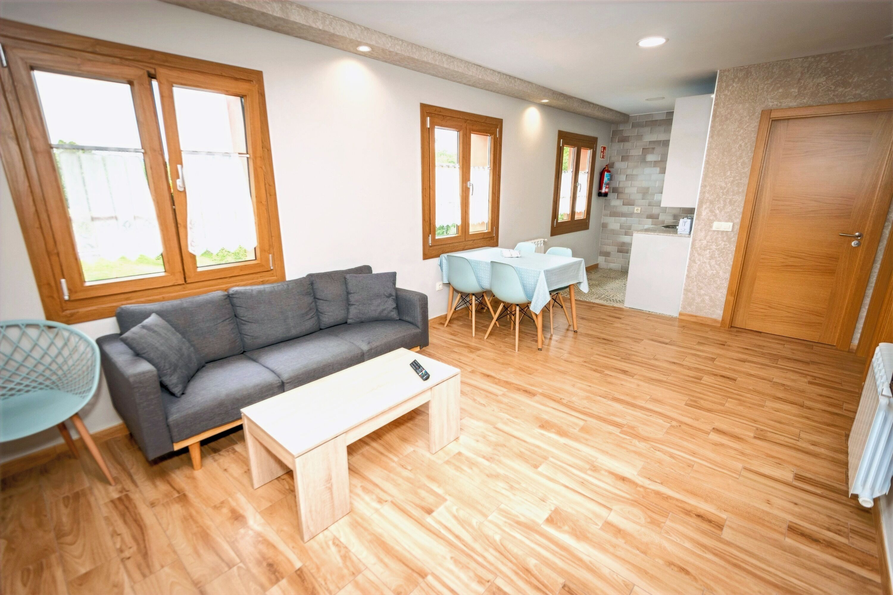 Una sala de estar moderna con un sofá gris, una mesa de centro blanca y un comedor con mesa y sillas.