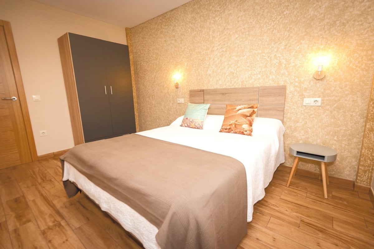 Un dormitorio con cama, armario de madera y dos luces fijadas a la pared.